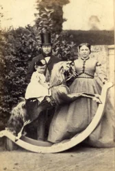 Jeune fille sur un grand cheval à bascule avec un homme et une femme debout, années 1860